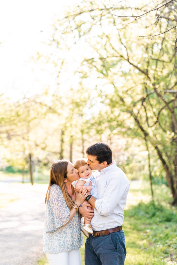 Chattanooga Family Photographer; 6 month milestone photos at Renaissance Park Chattanooga, TN - golden hour photography - Photo shoot outfits white and blue - Family of 3 posing- kissing baby