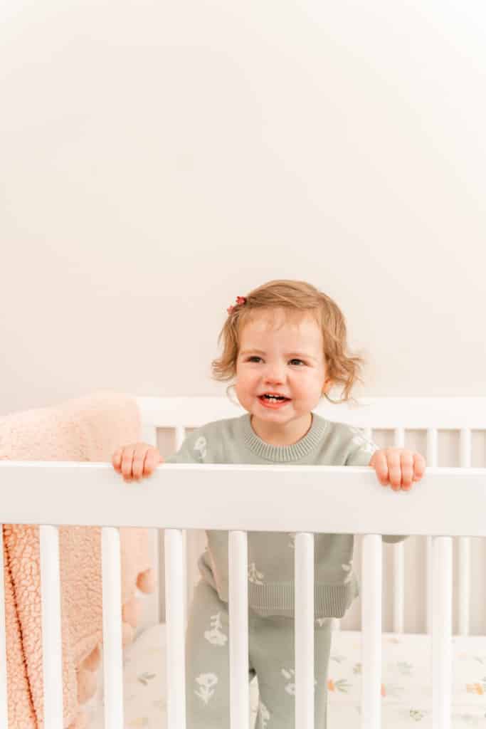 Toddler girl standing in crib during family photographs taken with flash