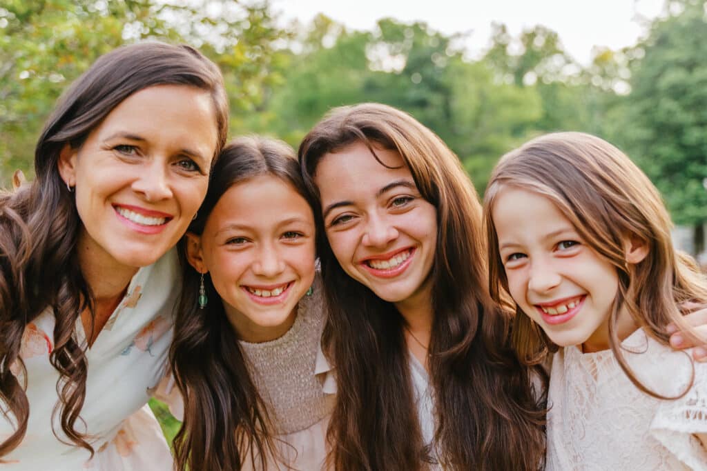 Mother and daughters smile naturally at camera.
