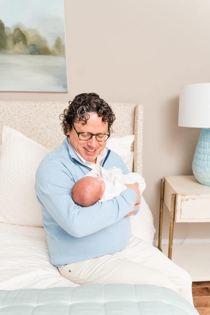 Father cuddling son during newborn photography session, white and light blue newborn photography session
