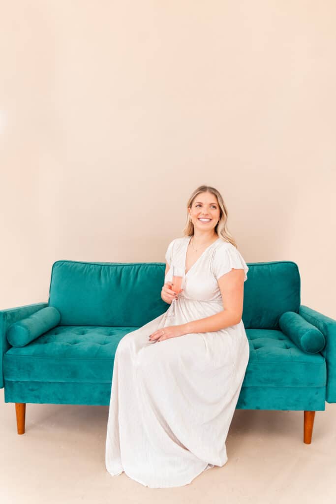 Model sitting on green sofa wearing cream Christmas party dress