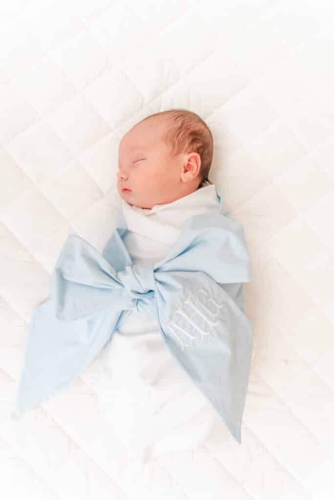 Swaddled baby boy with blue ribbon swaddle during in home flash photography session