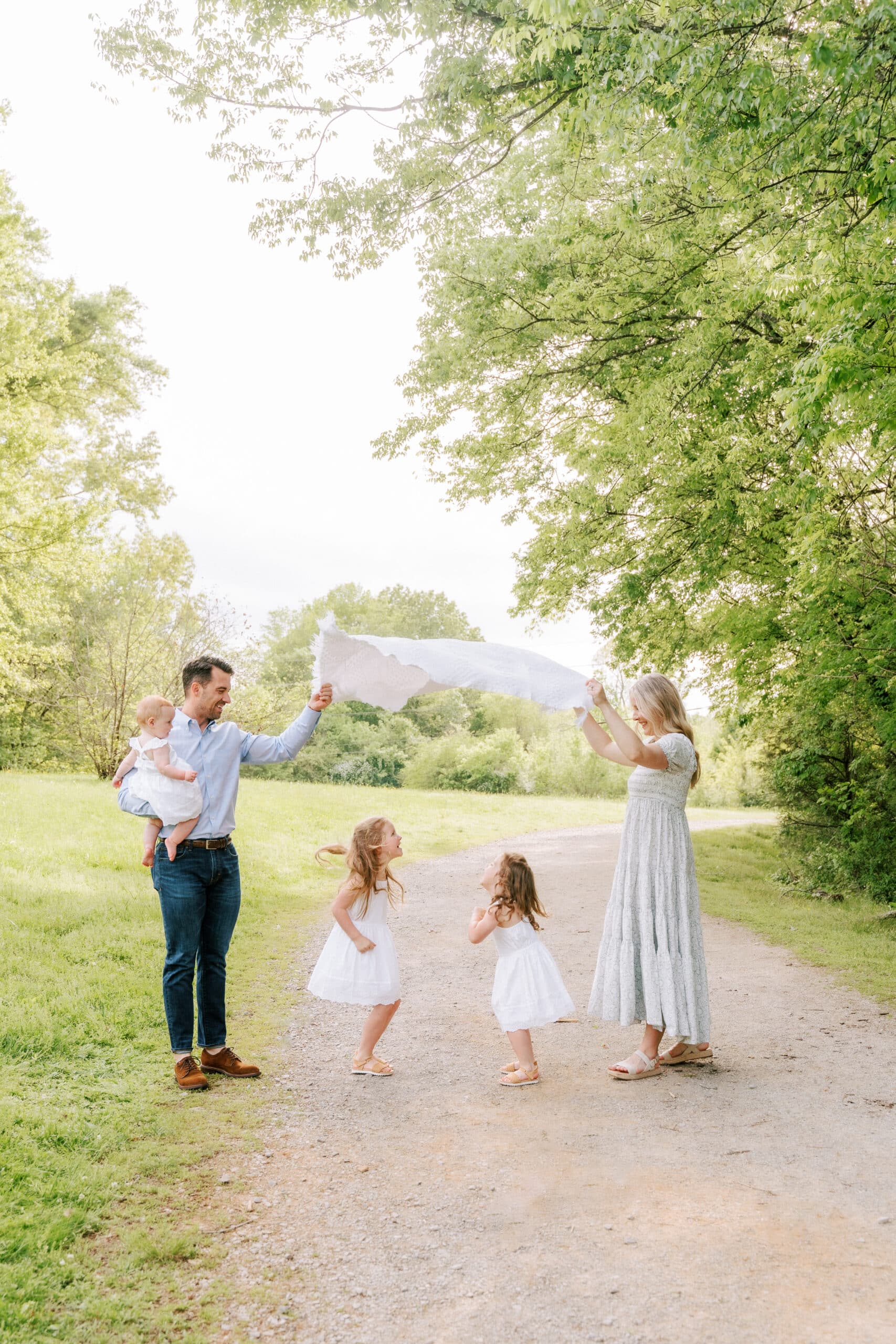 Family photography featuring entire family playing with blanket in park.