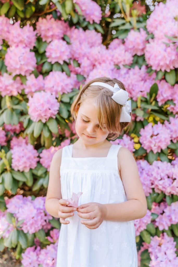 Child holds flower posing in front of spring blooms.