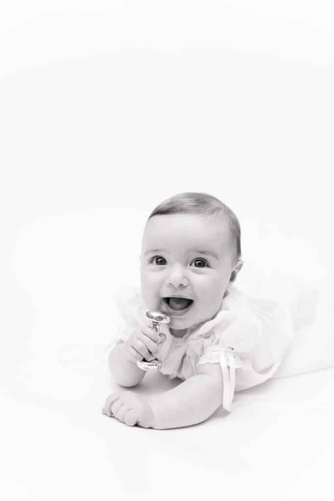 6 month old baby holds silver rattle in black and white traditional portrait