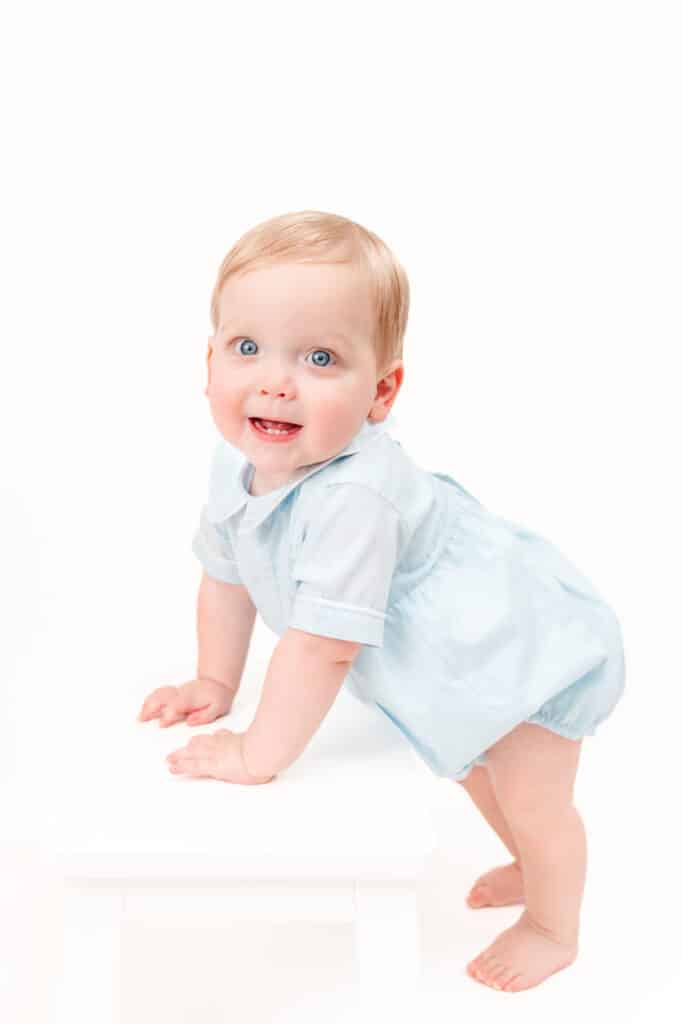 Little boy supports self on white stool during heirloom photo session