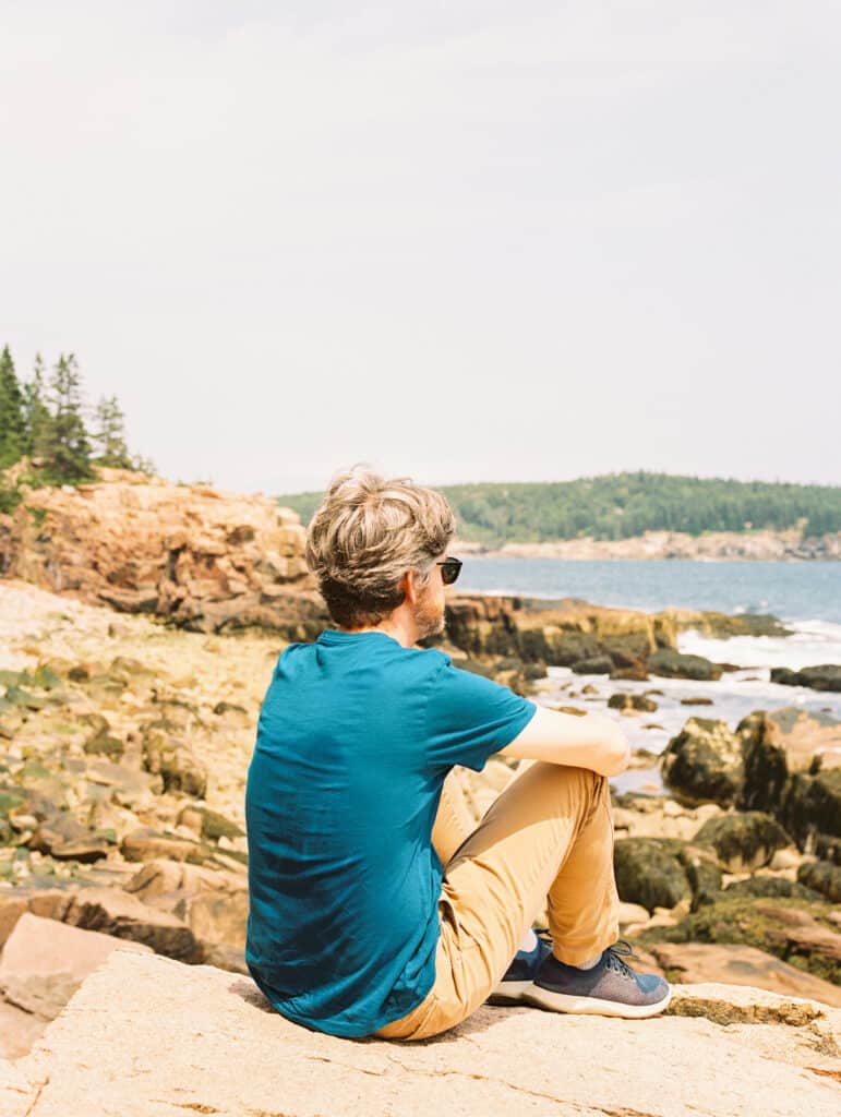 Man sits and looks out over ocean and rocky cliffs at Acadia National Park