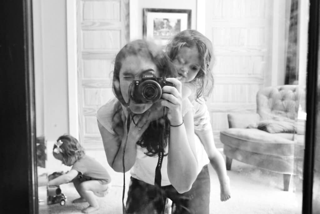 Photographer Kelley Hoagland takes picture of herself and her daughter in the mirror. See the aperture opening in the front of her lens.