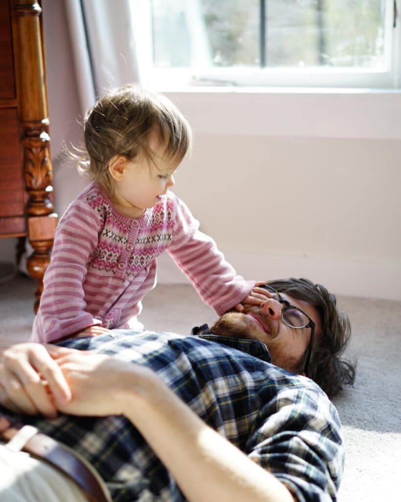 Candid photos of baby girl climbing on father who is laying on carpet.  Photographer learned to take better photos by practicing every week at home. 