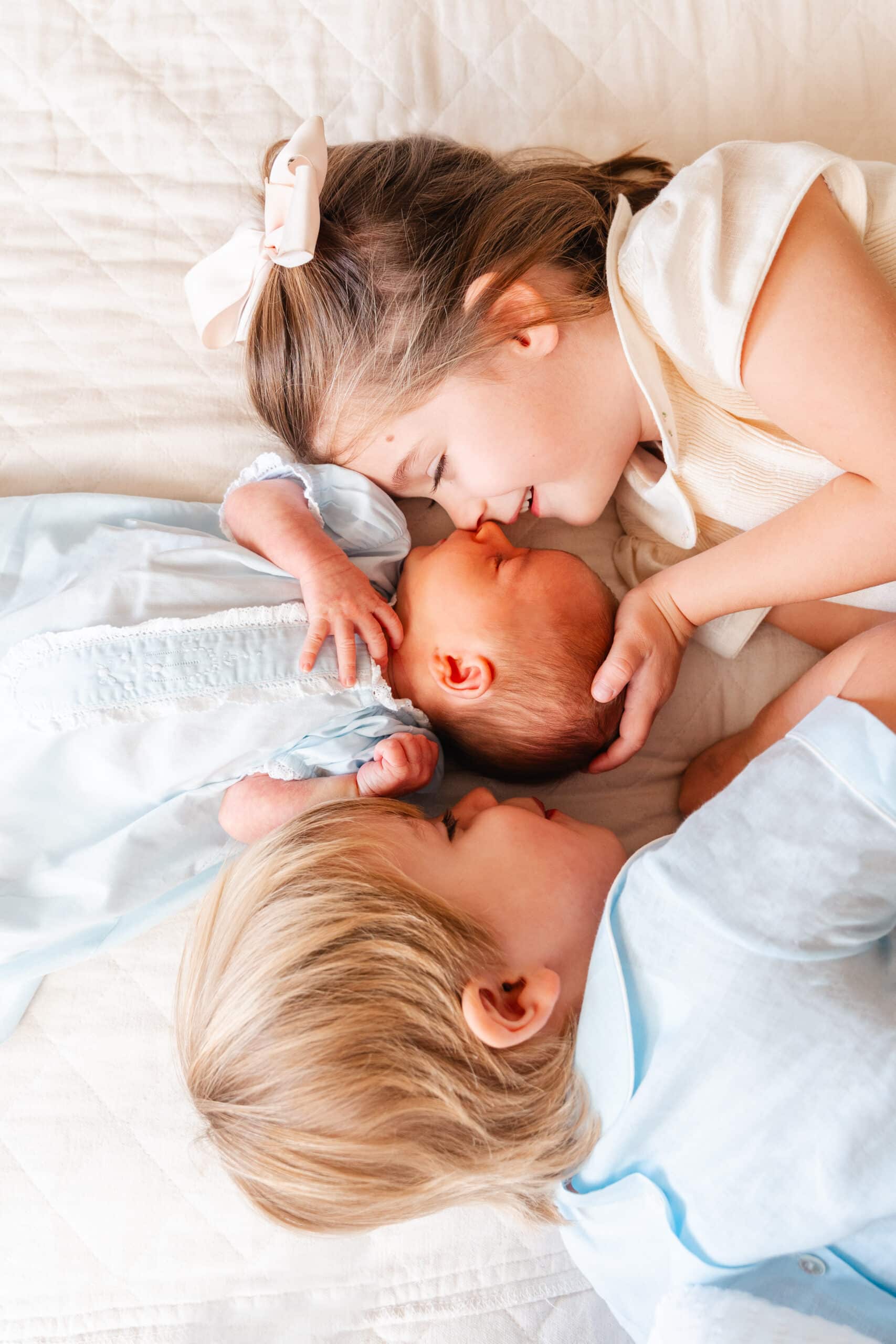 Image of older brother and sister snuggling newborn brother