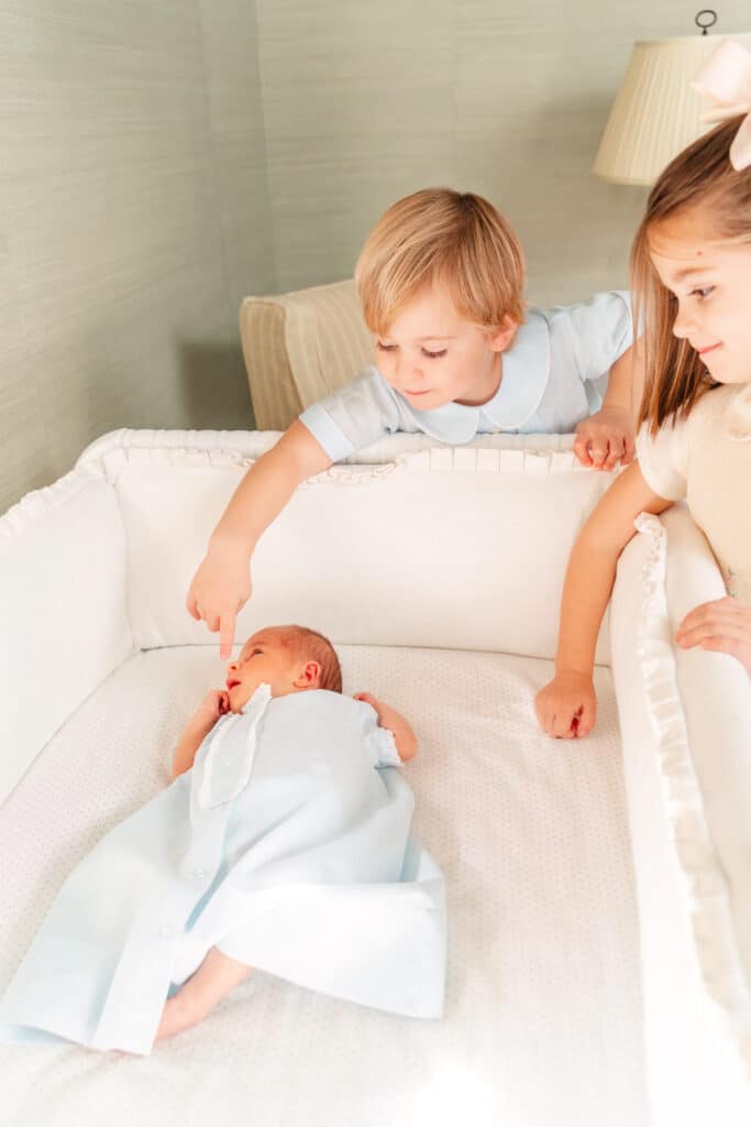 Older siblings look down at baby brother in crib.