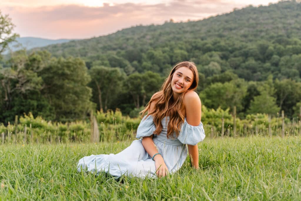 When do you take senior pictures? Senior girl sits in the grass and smiles at the camera during spring session.