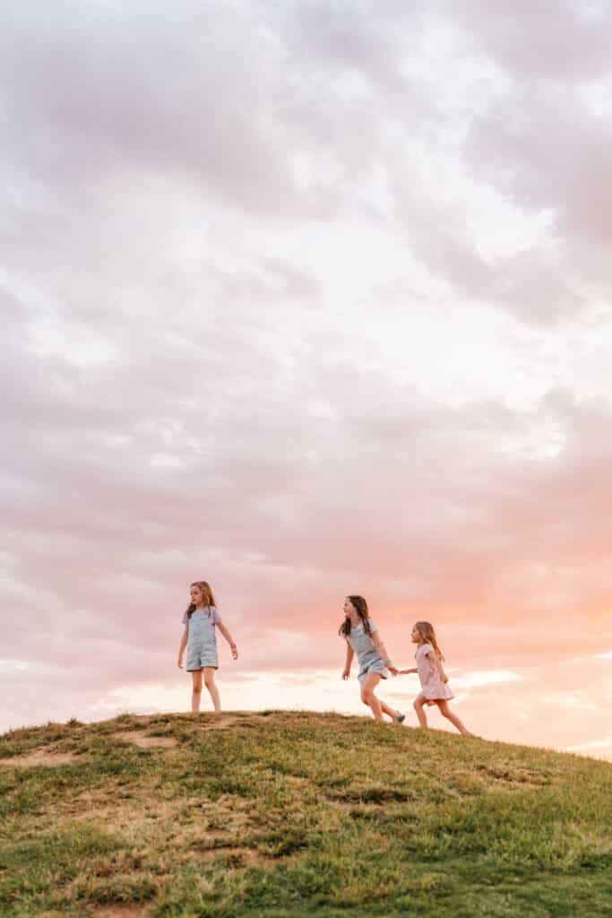 Portrait of 3 daughters playing on hill at sunset.